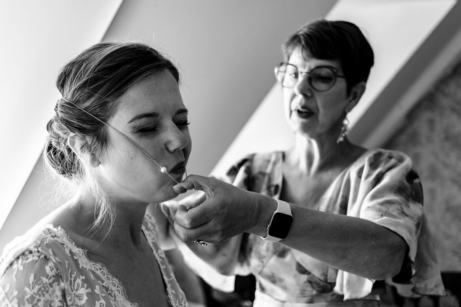 Photo drole de la maman de la mariée qui lui passe un collier lors des préparatifs du mariage au chateau d'osthoffen